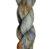 Skein of hand dyed fingering weight yarn in the color grey orange black speckles