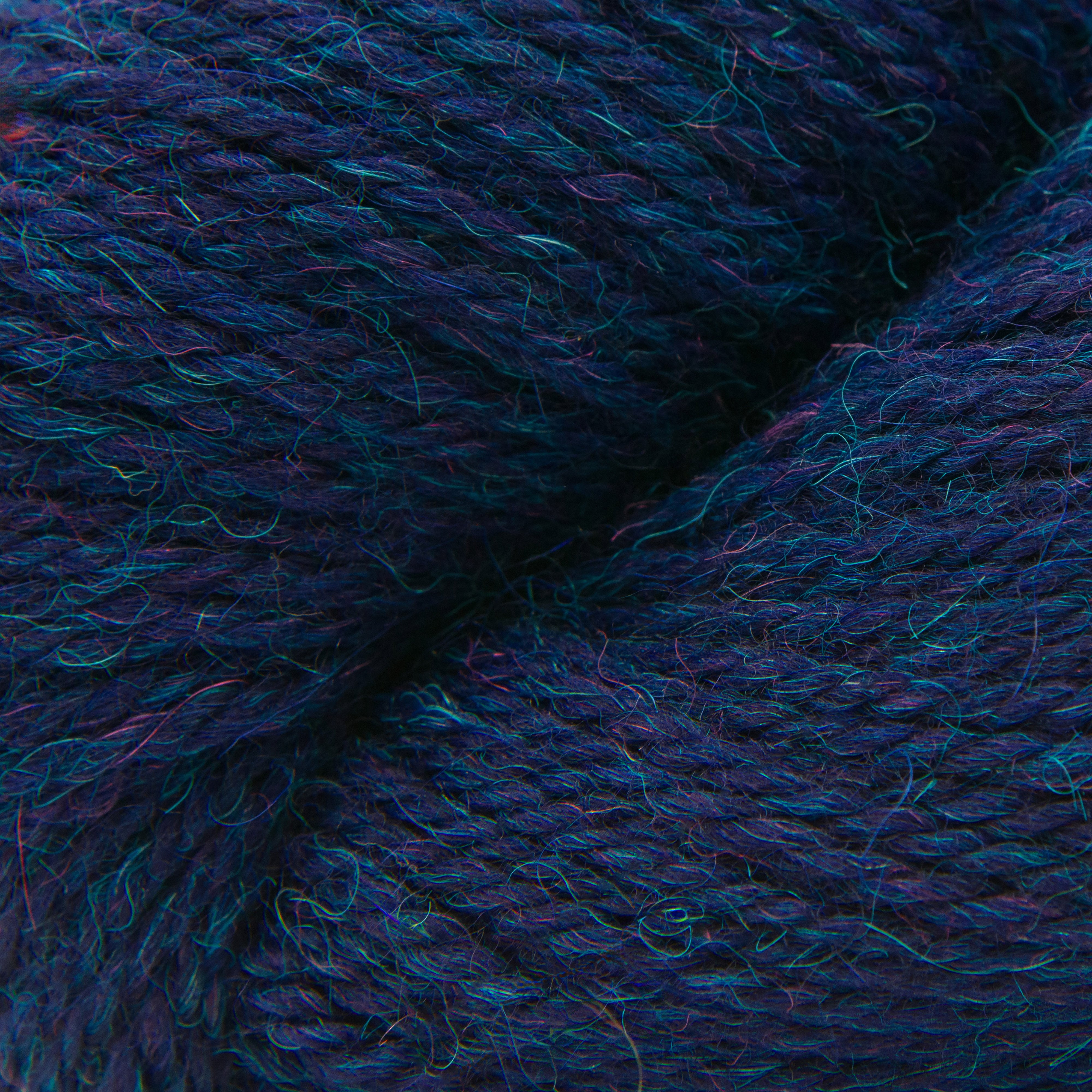 A close-up of textured yarn with a variegated colorway of deep navy, purple, and bright teal blue.