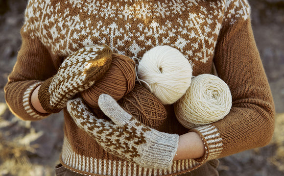 Person wearing a brown sweater and patterned gloves holding yarn balls.