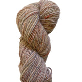 A single skein of variegated yarn with soft, fuzzy texture in muted beige, brown, and peach tones, photographed on a plain off-white background.