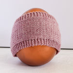 A dusty pink hand-knit beanie hat displayed on a brown mannequin head against a plain white background.