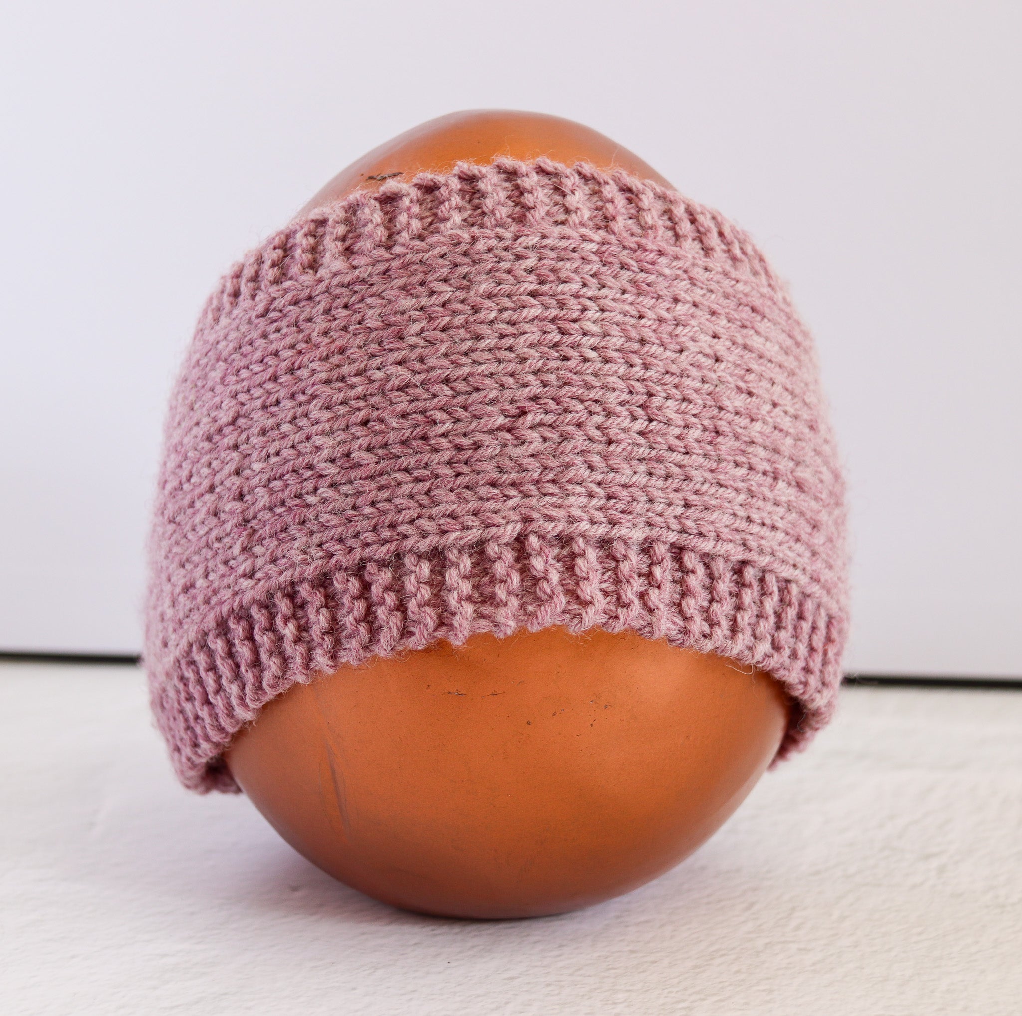 A dusty pink hand-knit beanie hat displayed on a brown mannequin head against a plain white background.