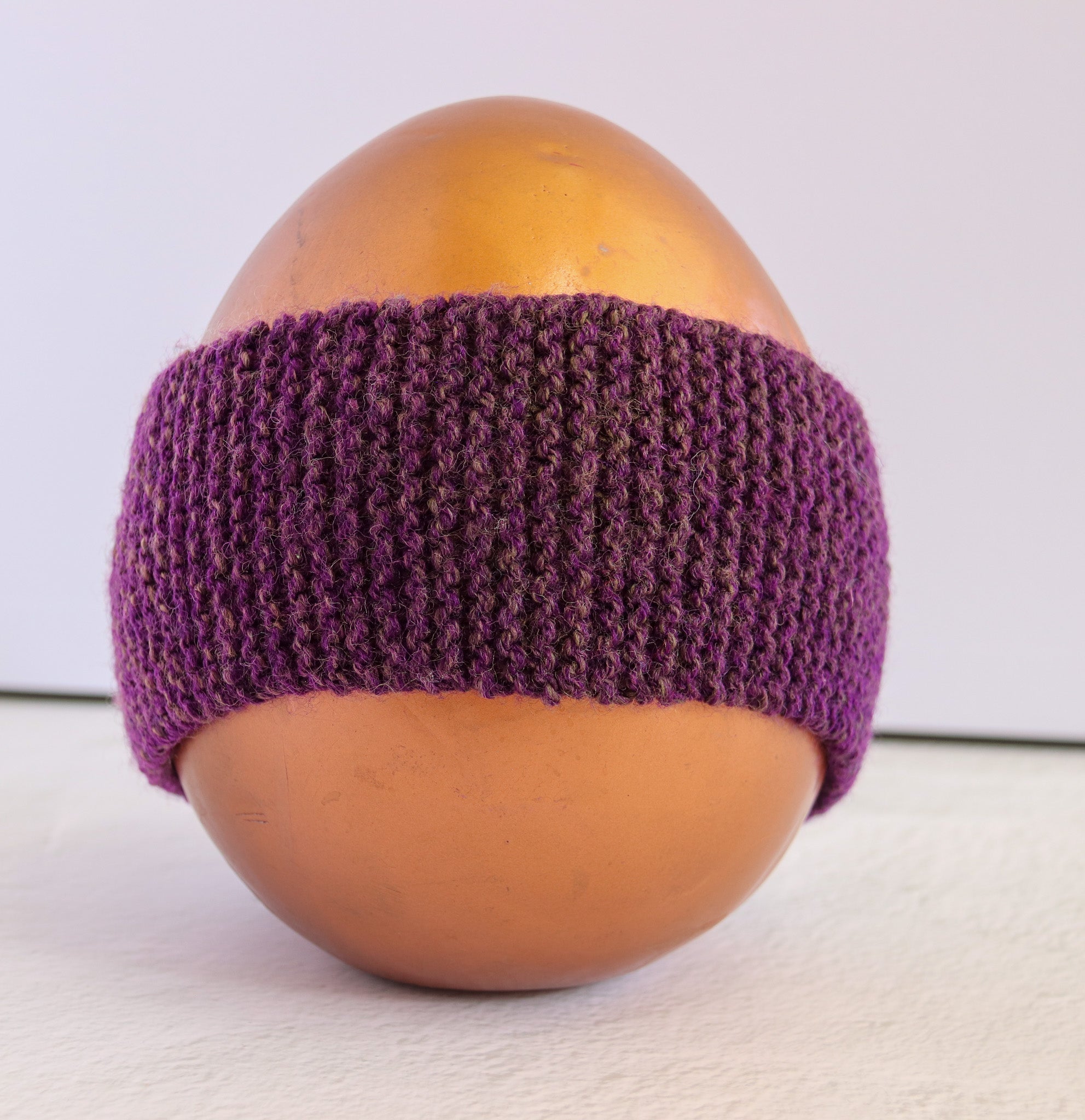 A purple knitted headband displayed on a glossy gold mannequin head against a plain light background.