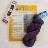 A knitted sock kit laid out on a white textured fabric background, including a package of KnitPei ginger yarn, a book or booklet titled 'Knitting Pure & Simple Beginner Socks,' a blue Vintage Blue yarn skein, and a large purple yarn skein.