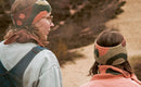 Two people wearing knitted headbands and scarves outdoors on a path.