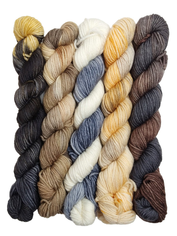 Photo of five mini hanks of yarn inspired by Melange. From left to right, the colors are:
-Variegated black with streaks of light yellow
-Variegated tan and white
-Striped white and gray-blue
-Variegated light yellow
-Striped brown and gray