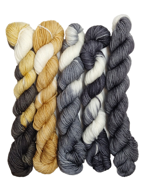 Photo of five mini hanks of yarn inspired by Puppy LuLu. From left to right, the colors are:
-Striped dark gray and variegated yellow/cream
-Yellow-tan with streaks of white
-Light gray with streaks of white
-Striped white and variegated dark gray
-Variegated gray