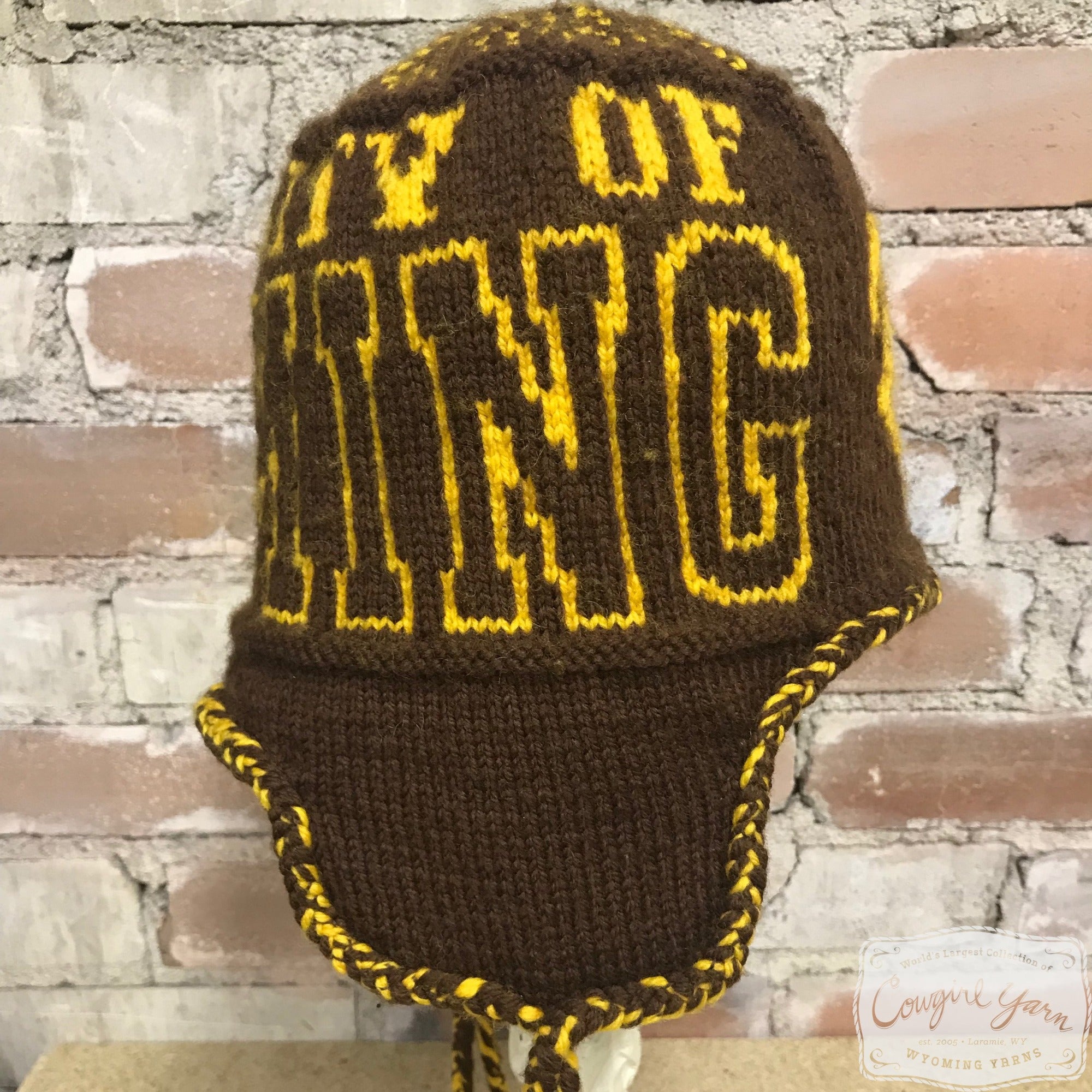 A brown knitted ski hat with the words University of Wyoming in gold styled against a brick wall.