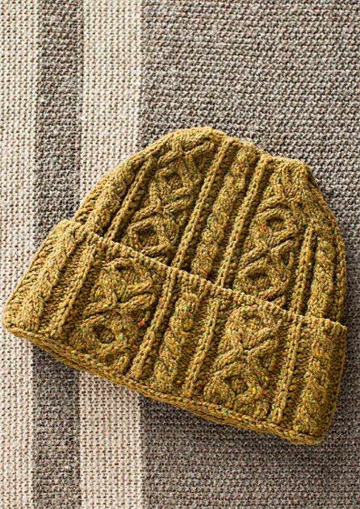 A knitted, cabled hat on a neutral background