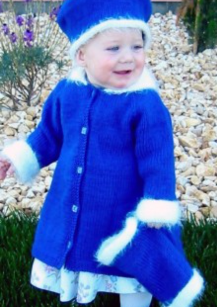 A toddler in a knitted coat, hat, and muffler set.