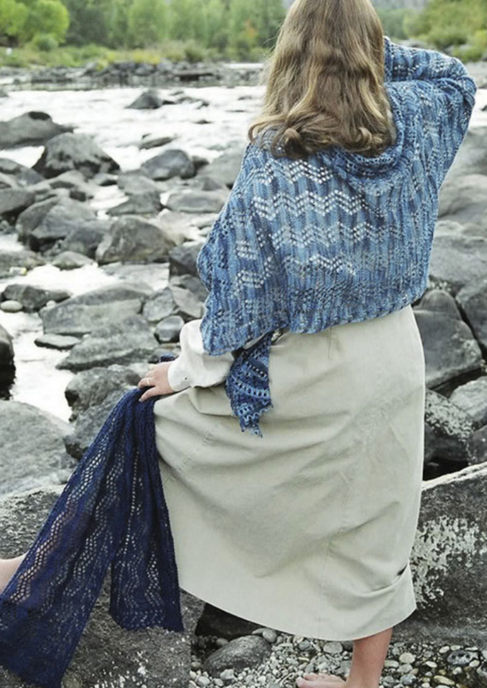 A woman wearing a knitted shawl and holding a scarf