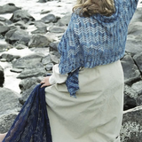 A woman wearing a knitted shawl and holding a scarf