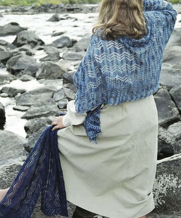 A woman wearing a knitted shawl and holding a scarf