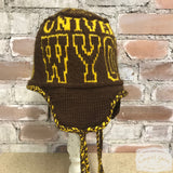 A brown knitted ski hat with the words University of Wyoming in gold styled against a brick wall.