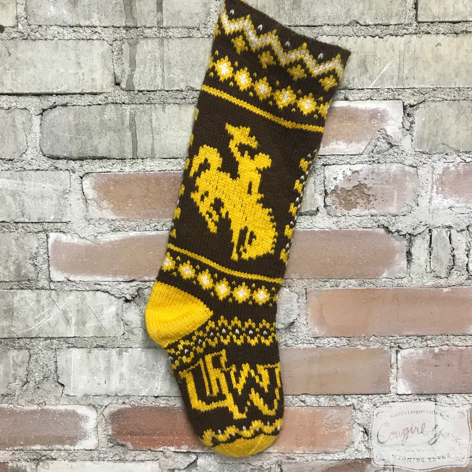 A brown and gold knitted stocking featuring the Steamboat icon hanging on a brick wall