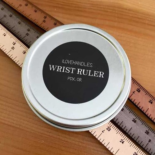 A photo of three wrist rulers under the metal tin case the rulers come in