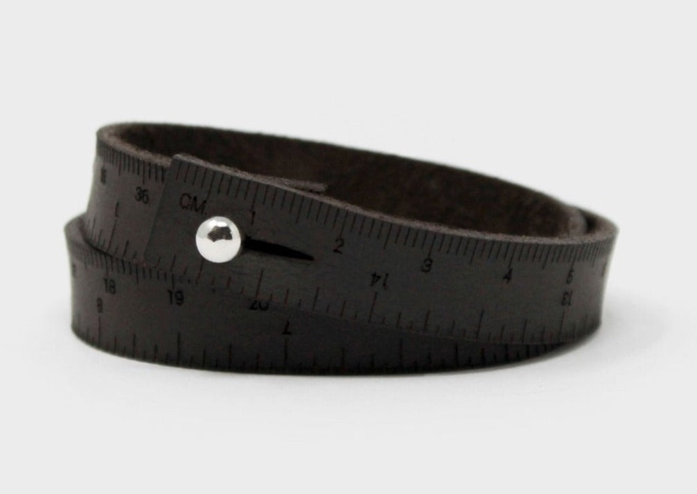 A photo of a dark brown wrist ruler with engraved measurements