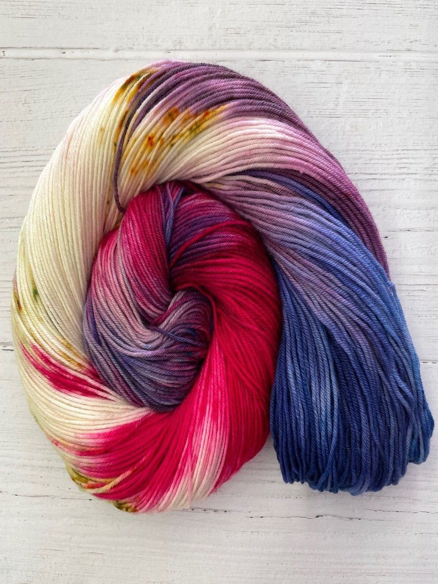 A skein of Knitted Wit's August Herstory, Partners in Crime. A cream skein with red, blue, and purple hues.