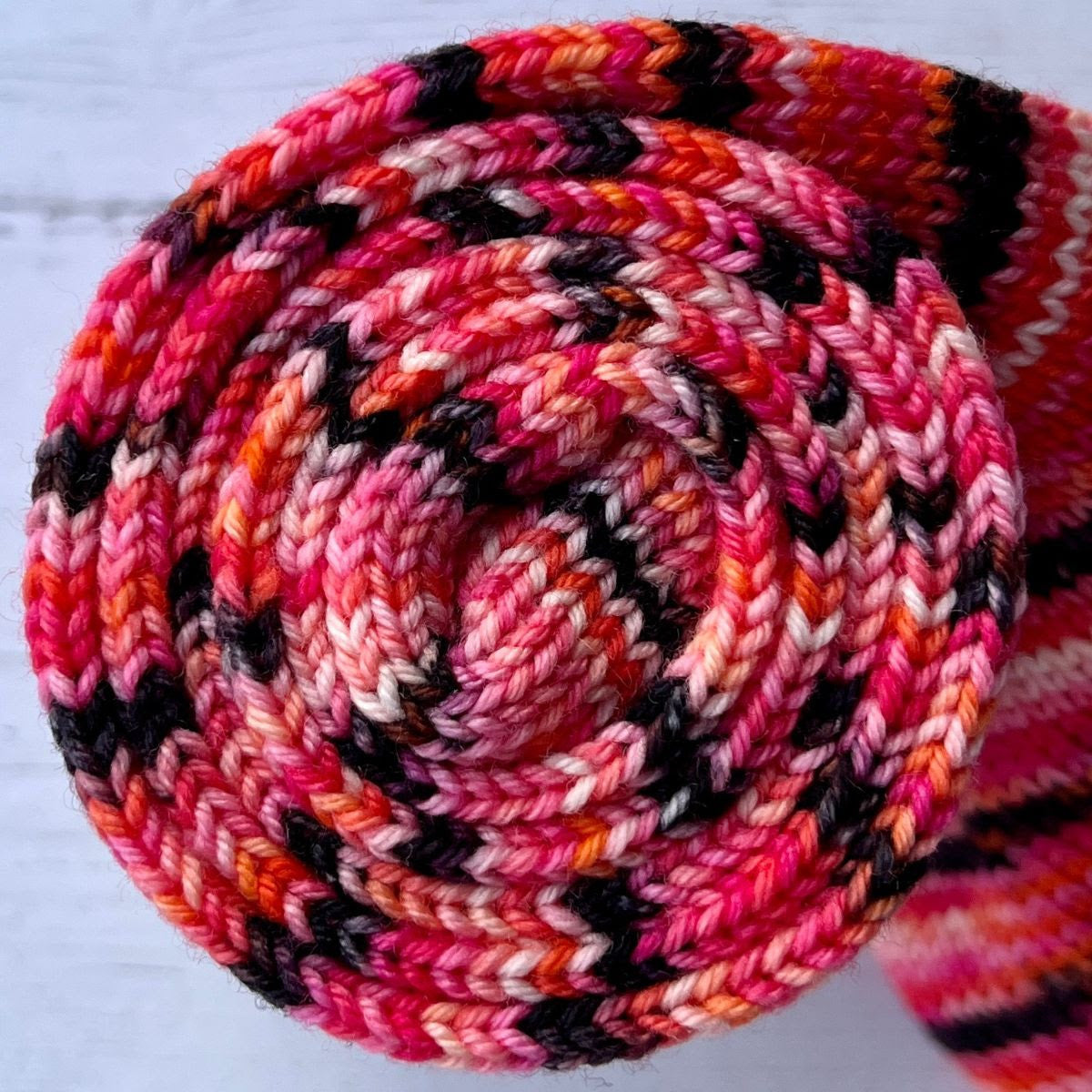 Feb 2023 Herstory: Lilith's Brood, a pink/black/orange in a sock tube, twisted into a spiral